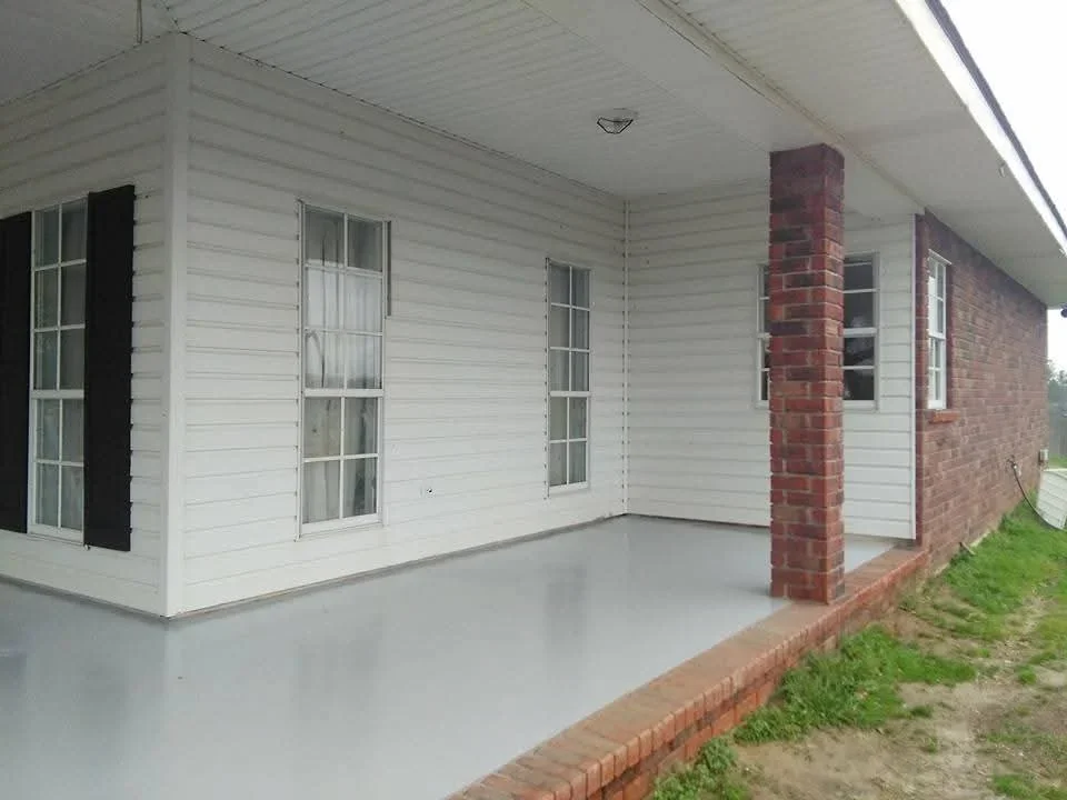 White painted house exterior with windows, brick chimney, and concrete foundation pad