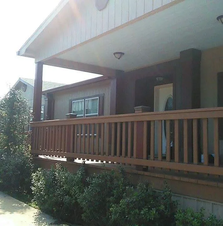 Covered porch with stained wood railing, metal roof overhang, and white soffit