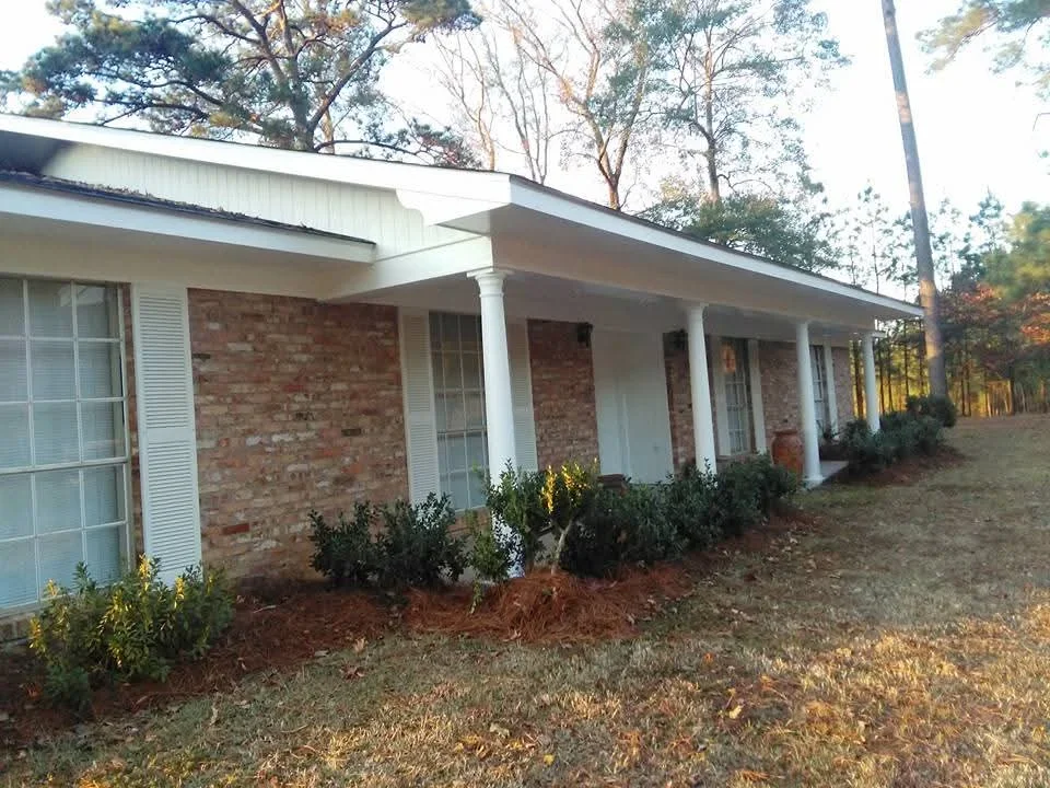 Brick home with white painted trim, columns, and fascia; landscaped front yard with mulch beds