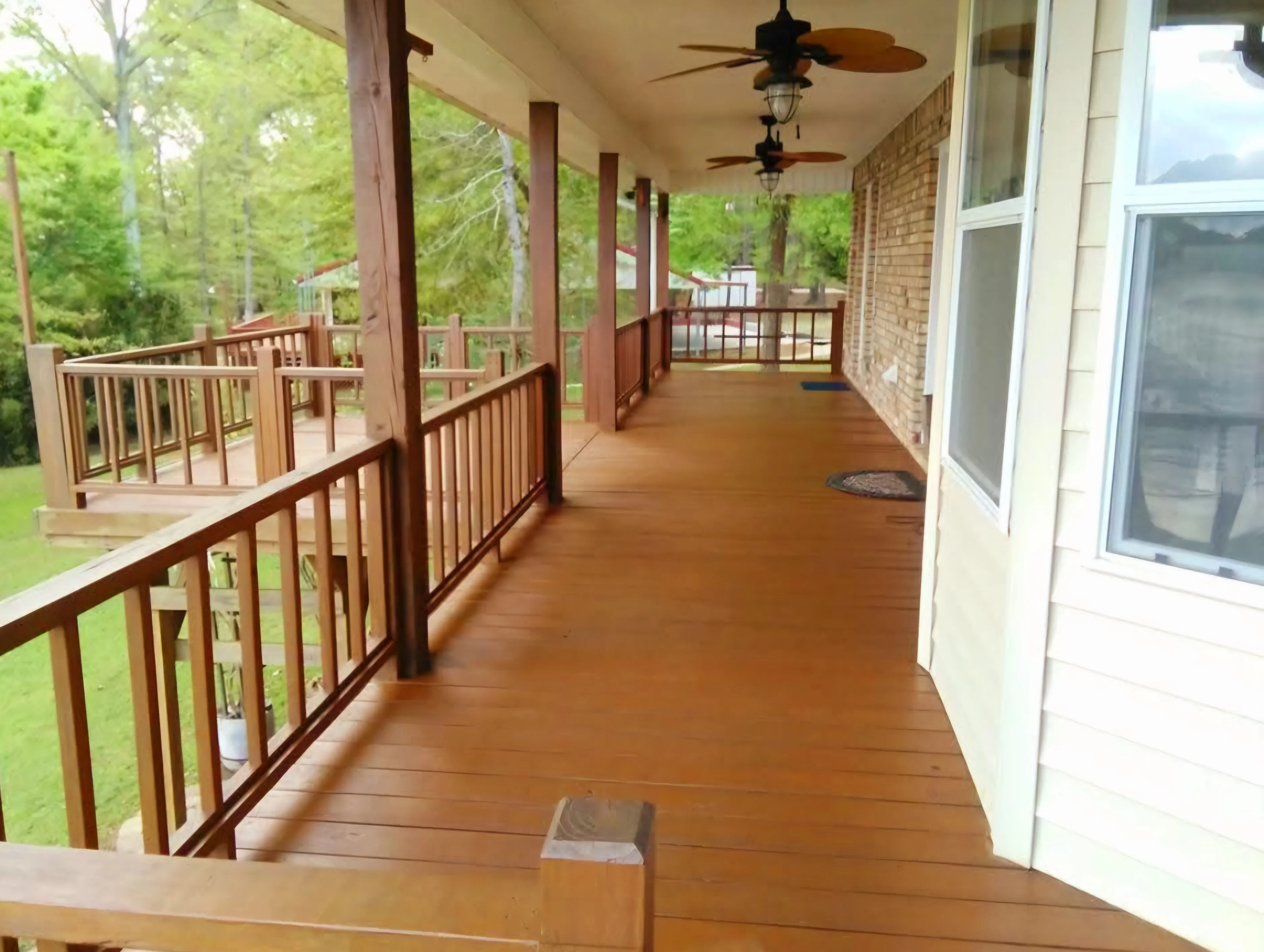 Stained wood deck with custom railings, covered ceiling, and ceiling fans overlooking wooded landscape