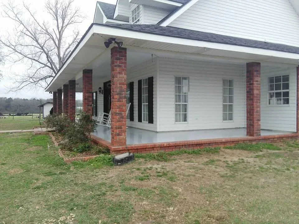 White painted house exterior with red brick columns and foundation trim, covered porch with windows