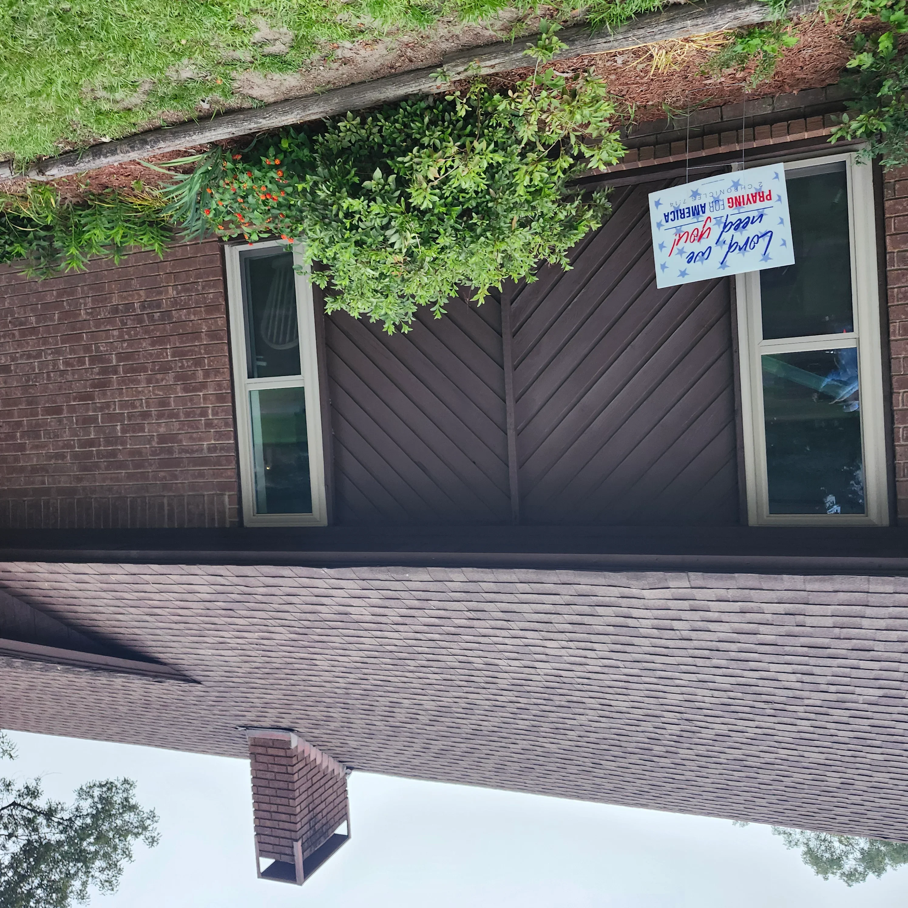 Dark painted garage door with diagonal panels, brick facade, and new soffit with hanging plants