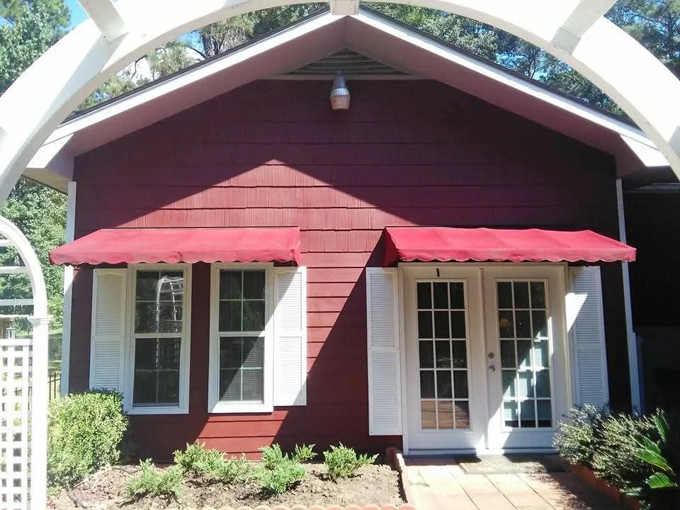 Burgundy painted cottage with cream trim, white shutters, and red fabric awnings over windows and door