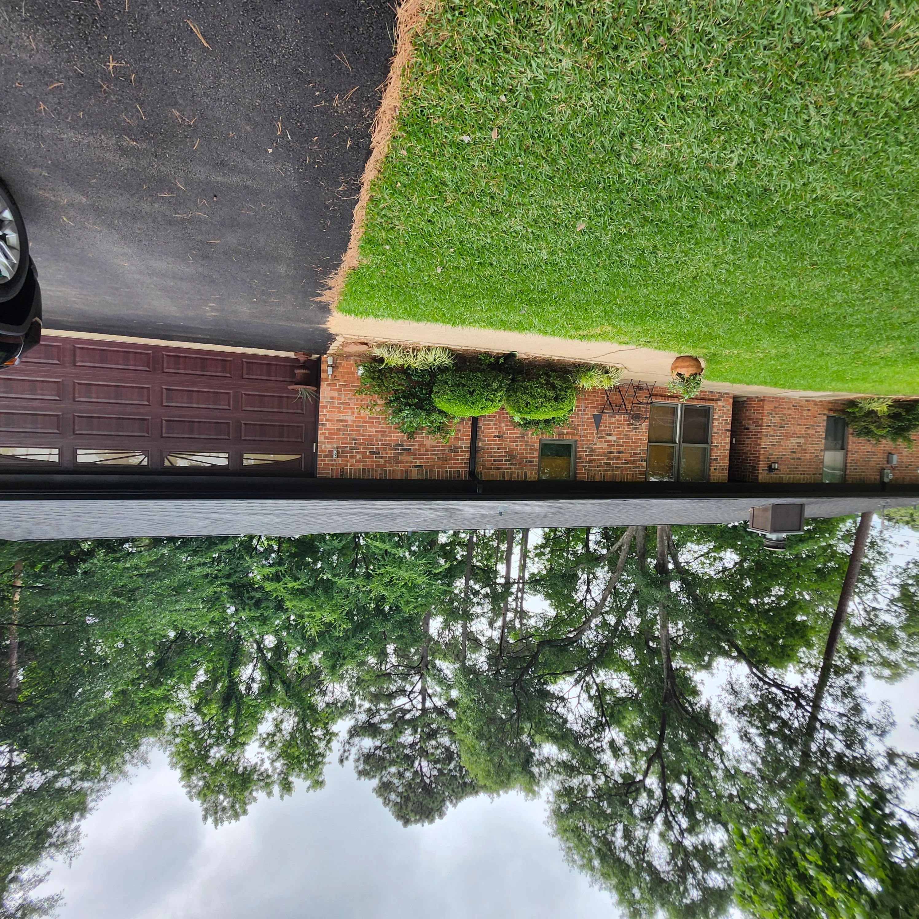 Newly coated asphalt driveway and freshly painted dark garage door on brick home