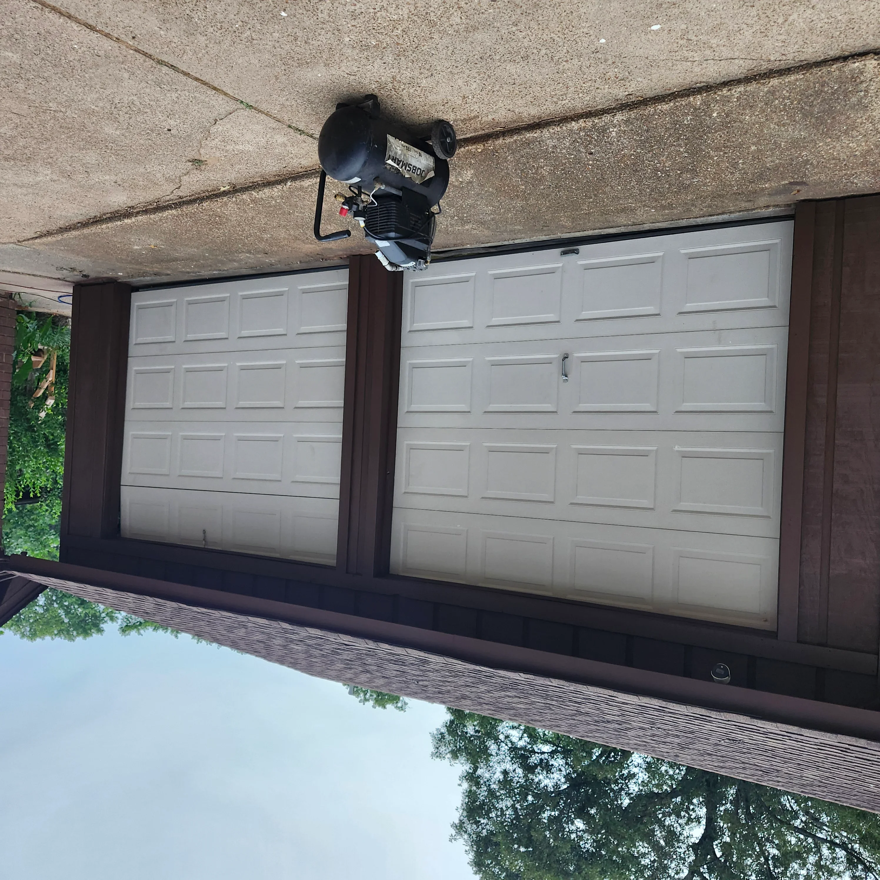 Two white raised-panel garage doors with dark brown trim and mounted garage door opener