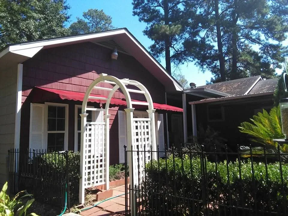 Burgundy and white painted cottage exterior with white lattice arbor entry and black metal fence