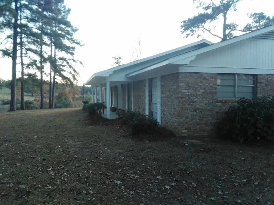 Brick ranch home with white trim, metal roof, and covered porch after exterior painting and coating work